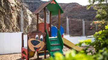 Une aire de jeux pour enfants avec un motif d’ours, un toboggan et une zone d’escalade, le tout installé sur une colline rocheuse.