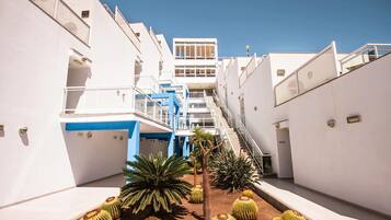 Un hôtel moderne doté d’une cour intérieure où l’on trouve des cactus et des palmiers, entouré de bâtiments blancs rehaussés d’accents bleus et agrémenté de nombreux balcons.