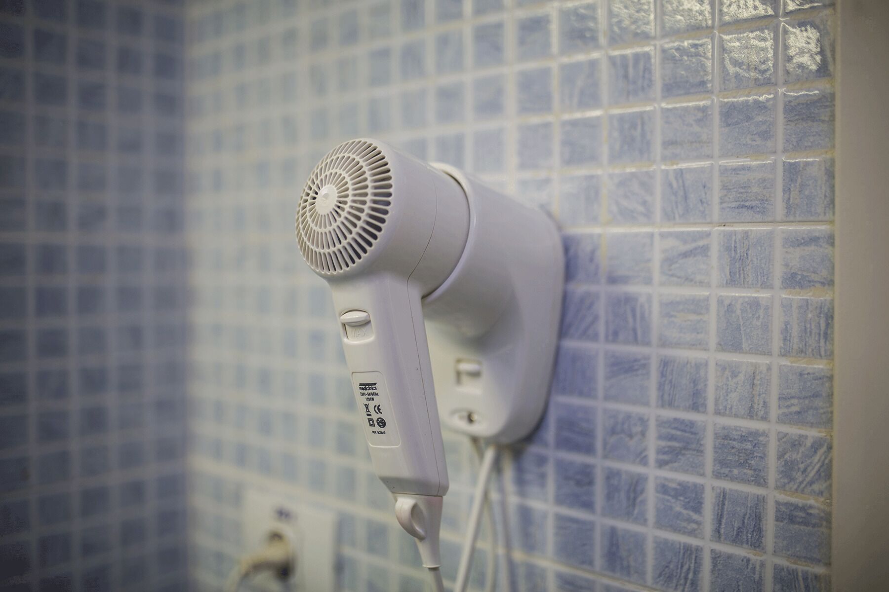 A hair dryer mounted on a tiled wall.