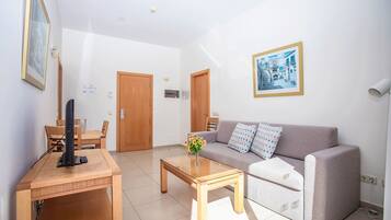 Una sala de estar con sofá, mesa de centro, televisor sobre un mueble y una puerta.