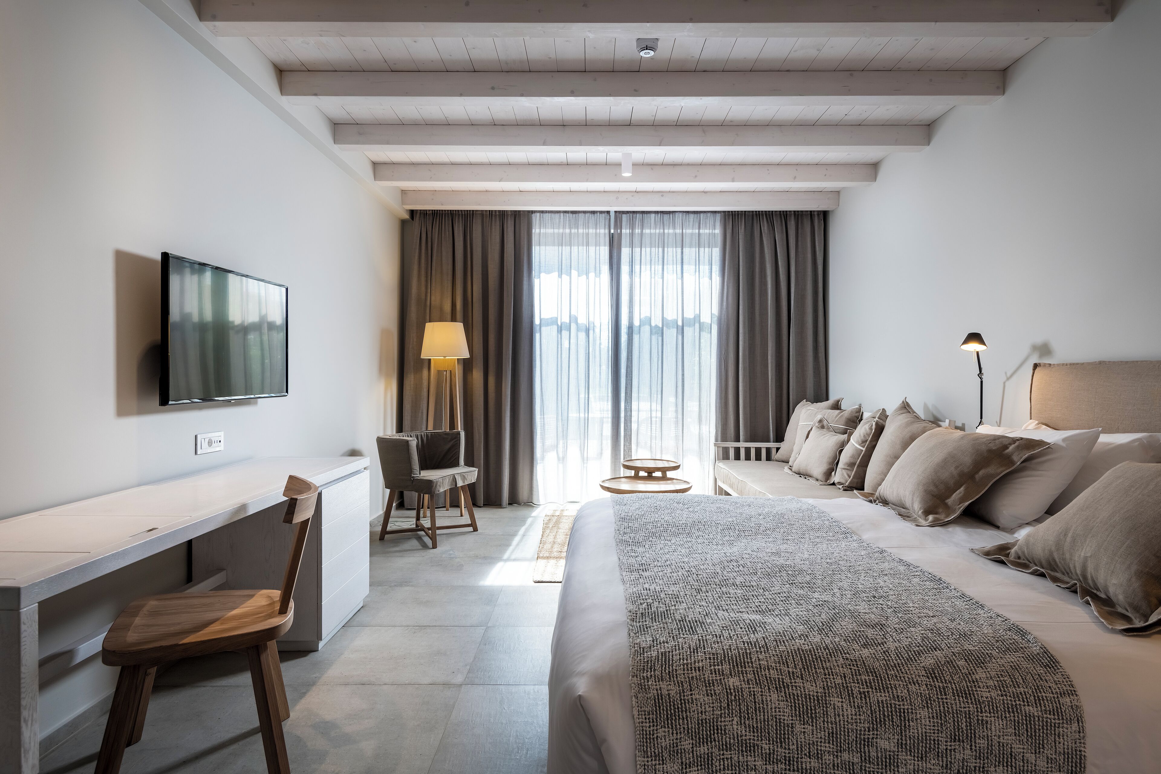 A modern hotel room with a bed, desk, chair, and a TV mounted on the wall.