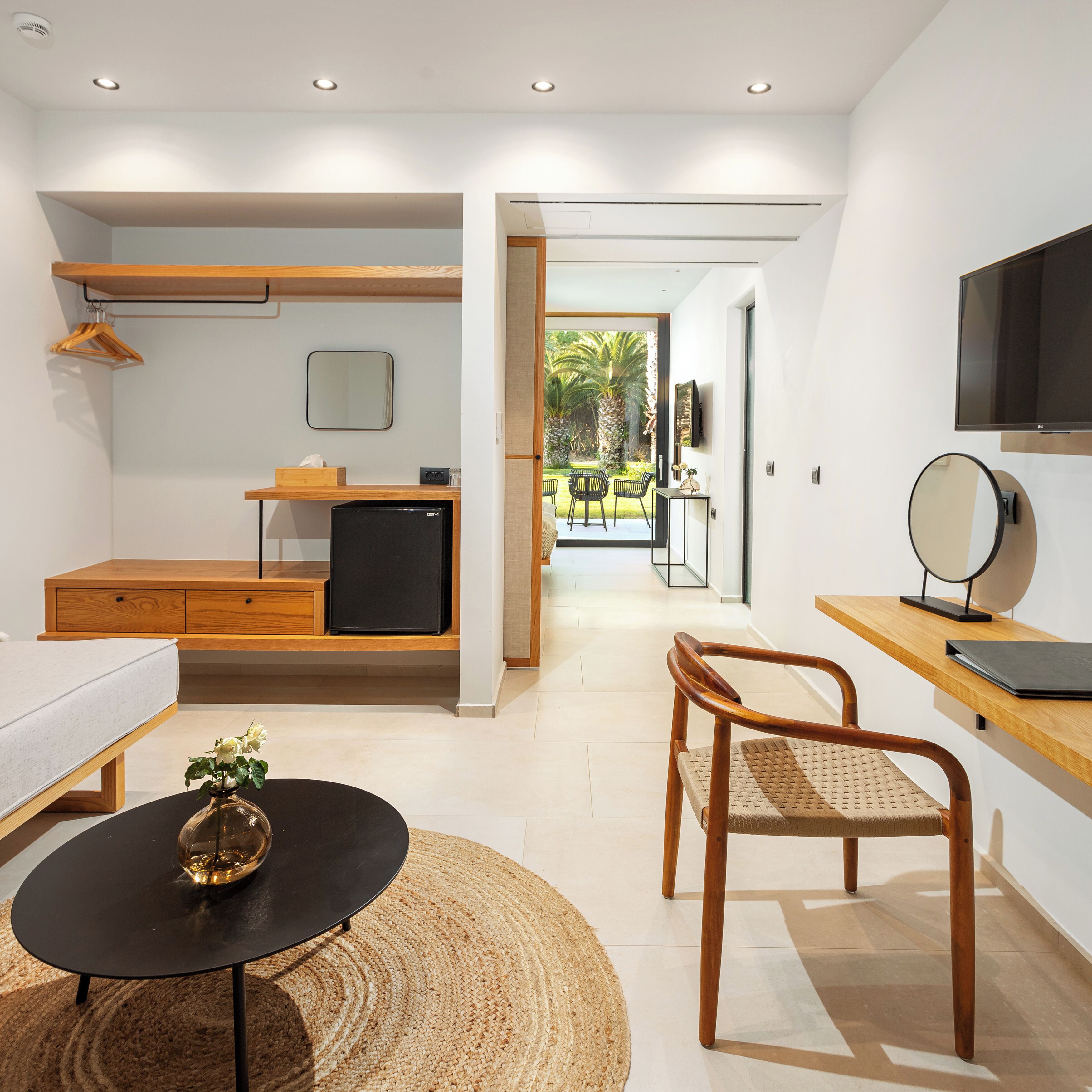 Una habitación de hotel moderna con cama, escritorio, silla, televisor pequeño y vistas al jardín.