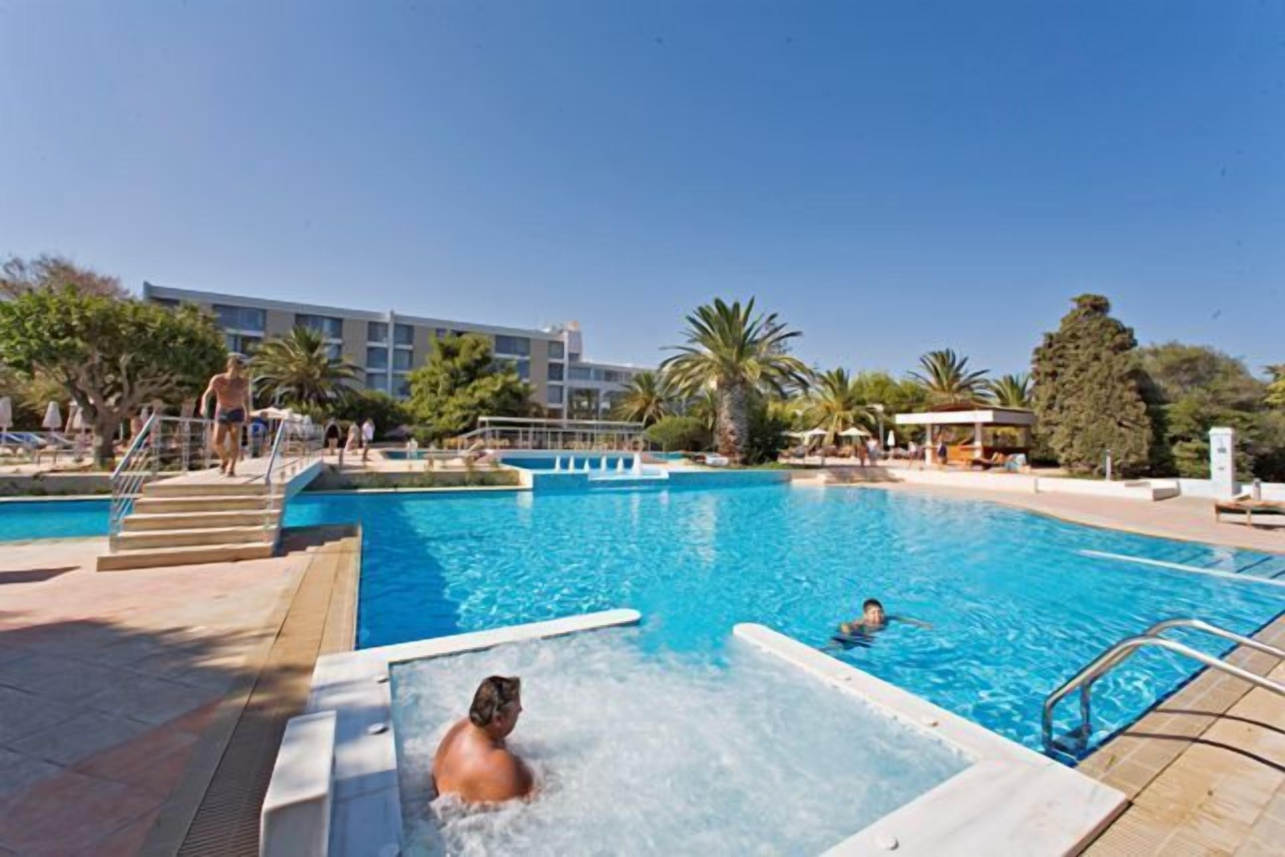 Un espace piscine comprenant un jacuzzi, des chaises longues et un bâtiment en arrière-plan.