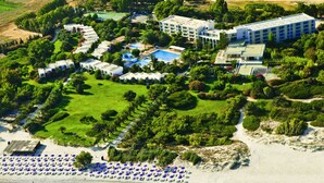 An aerial view of a resort with multiple buildings, a central pool area, and a beach with umbrellas. - Caravia Beach Hotel & Bungalows - All Inclusive (Kos)