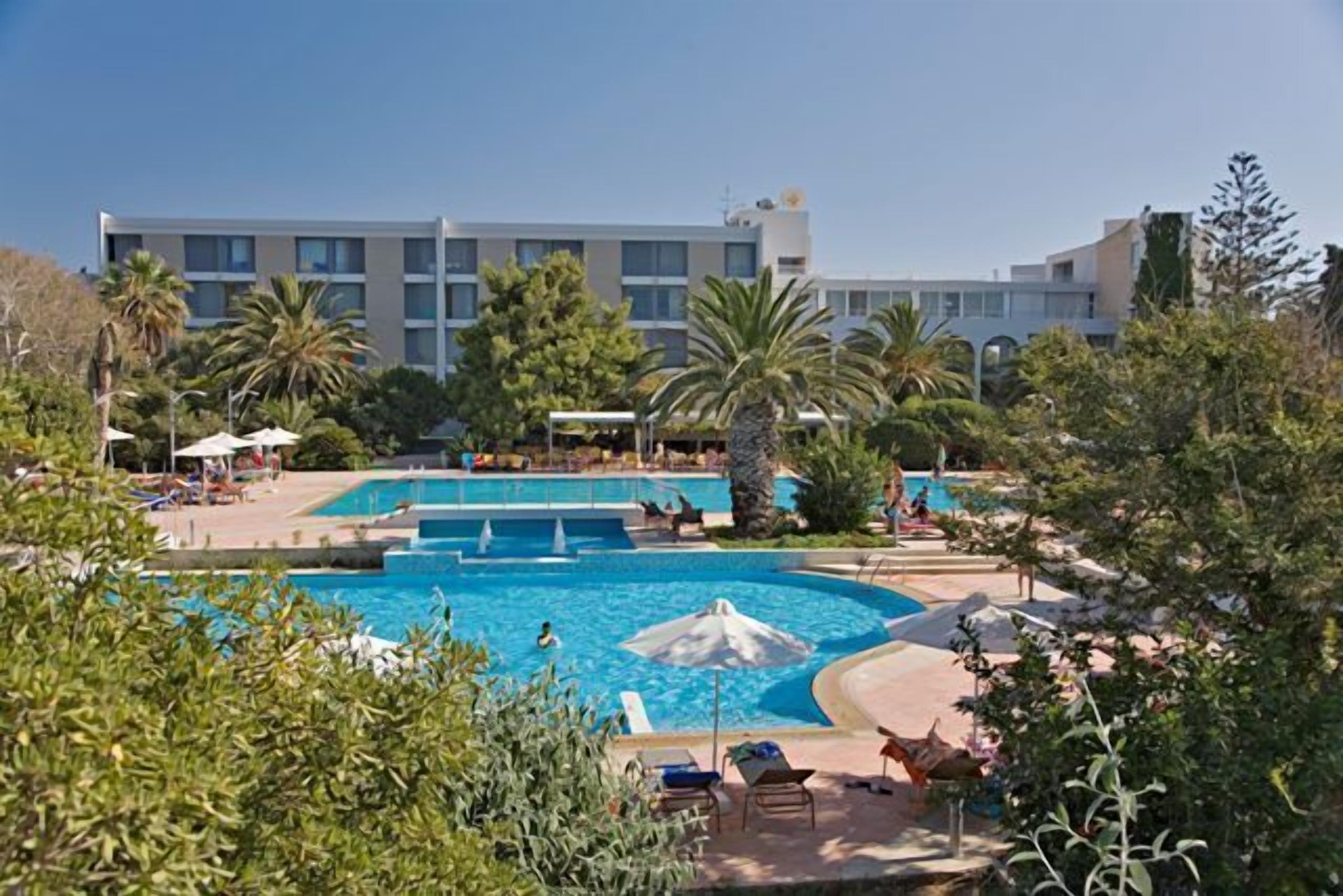 Um hotel com uma grande piscina ao ar livre rodeada por palmeiras e espreguiçadeiras.