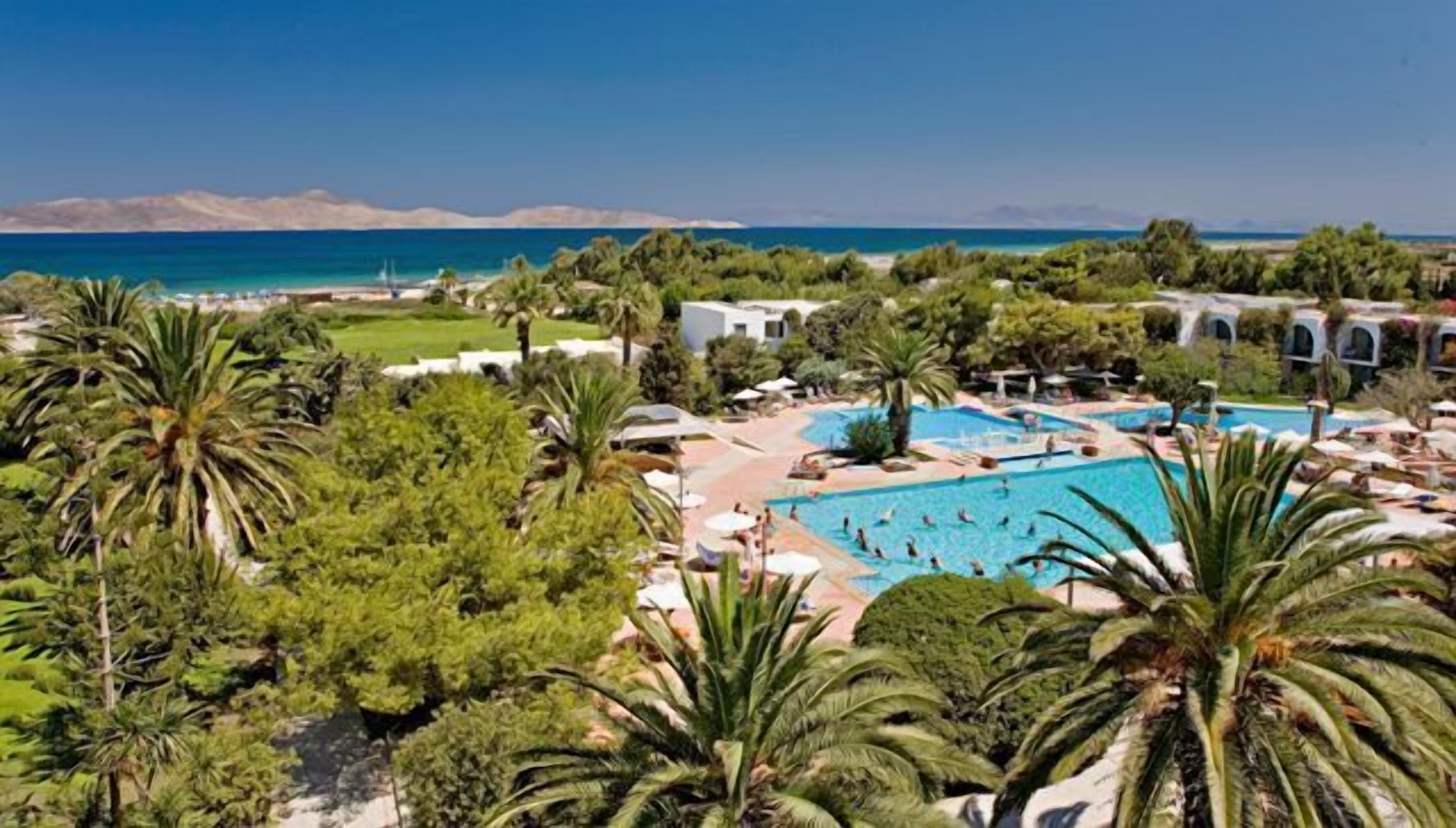 Um resort com uma piscina grande, palmeiras e vista para o mar.