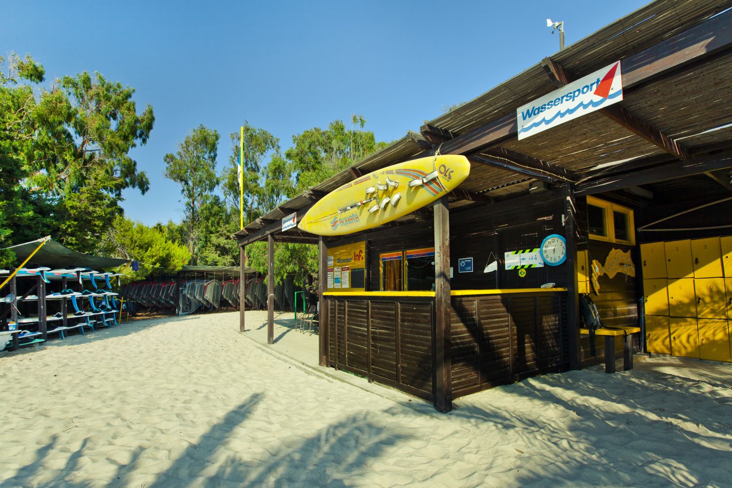 A beachside building with a surfboard sign, a clock, and lockers.