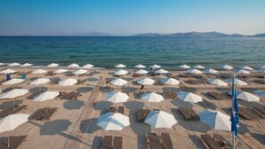 A beach with rows of sun loungers and white umbrellas, a clear sky, and calm sea. - Caravia Beach Hotel & Bungalows - All Inclusive (Kos)