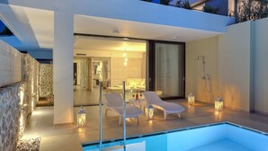 A modern outdoor pool area with lounge chairs and lanterns, a stone wall, and a view into the interior of a contemporary home. - Caravia Beach Hotel & Bungalows - All Inclusive (Kos)