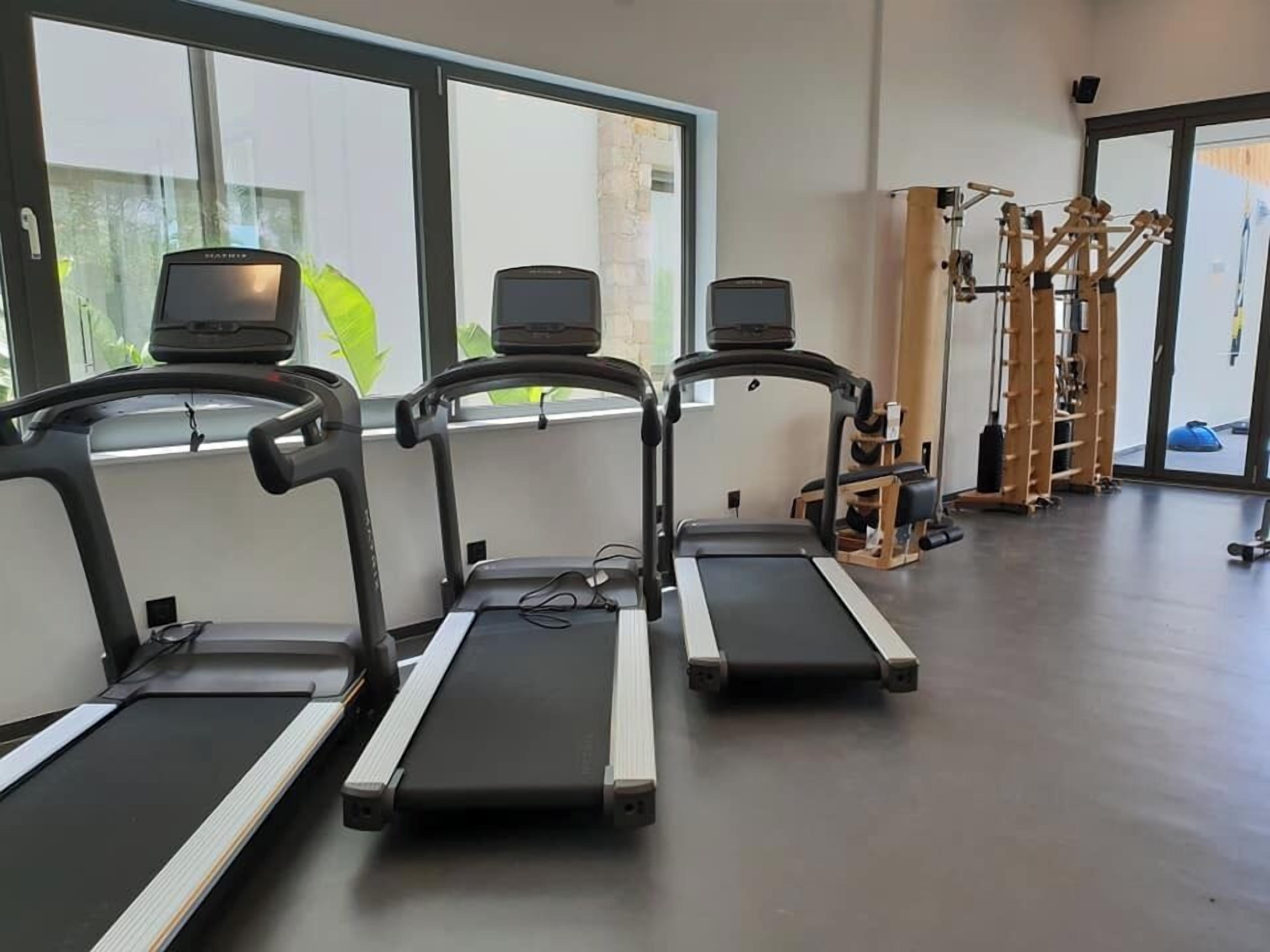 A gym with three treadmills aligned against a wall with large windows.
