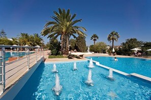 A swimming pool with multiple water jets, surrounded by palm trees and lounge chairs.