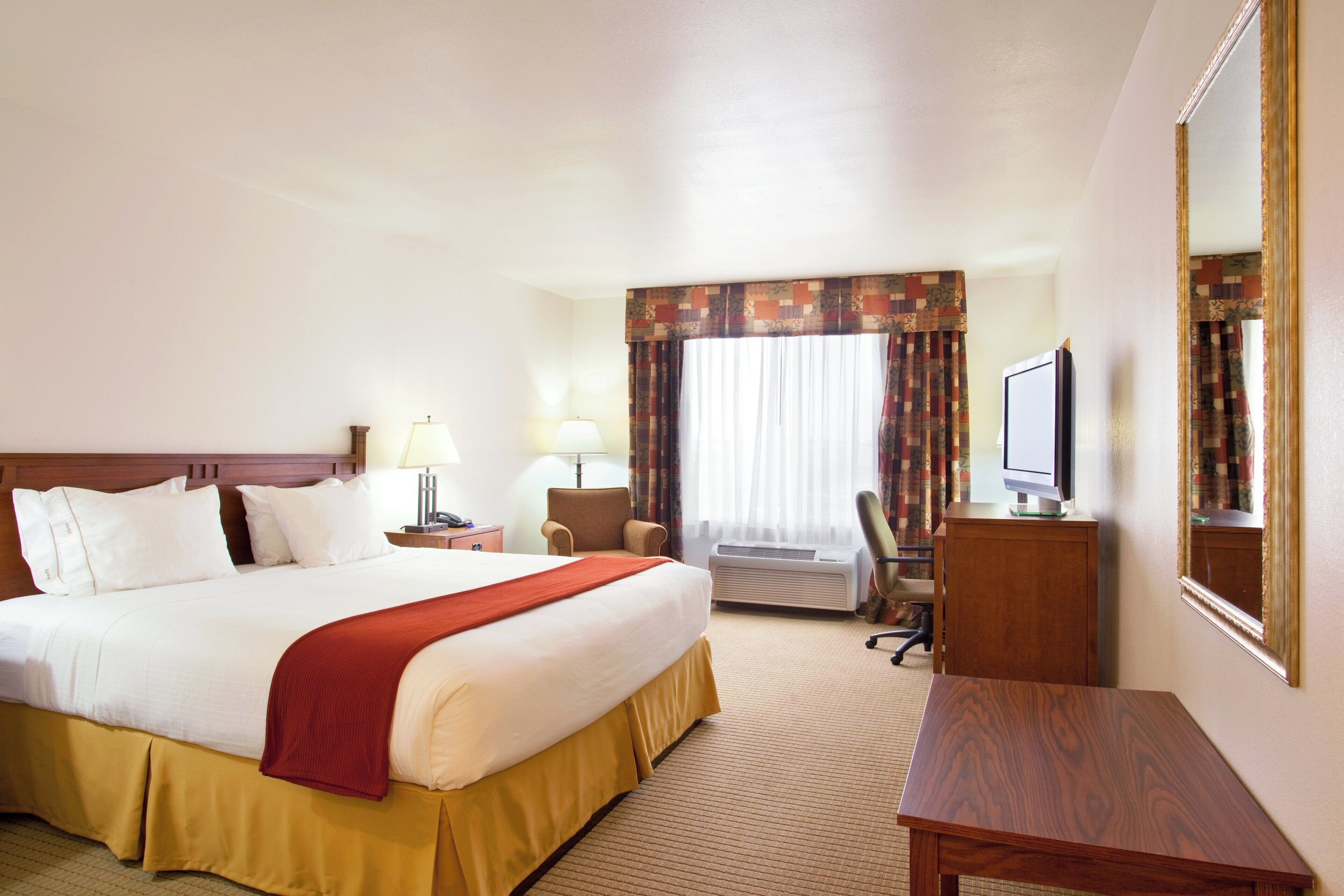 A hotel room with a large bed, two bedside tables with lamps, a desk with a computer, a chair, and a television.