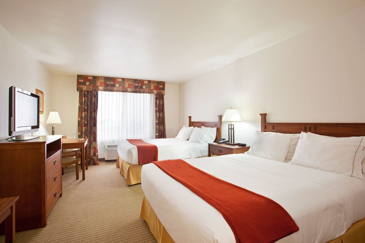 A hotel room with two beds, a desk, a chair, a television, and a window with curtains.