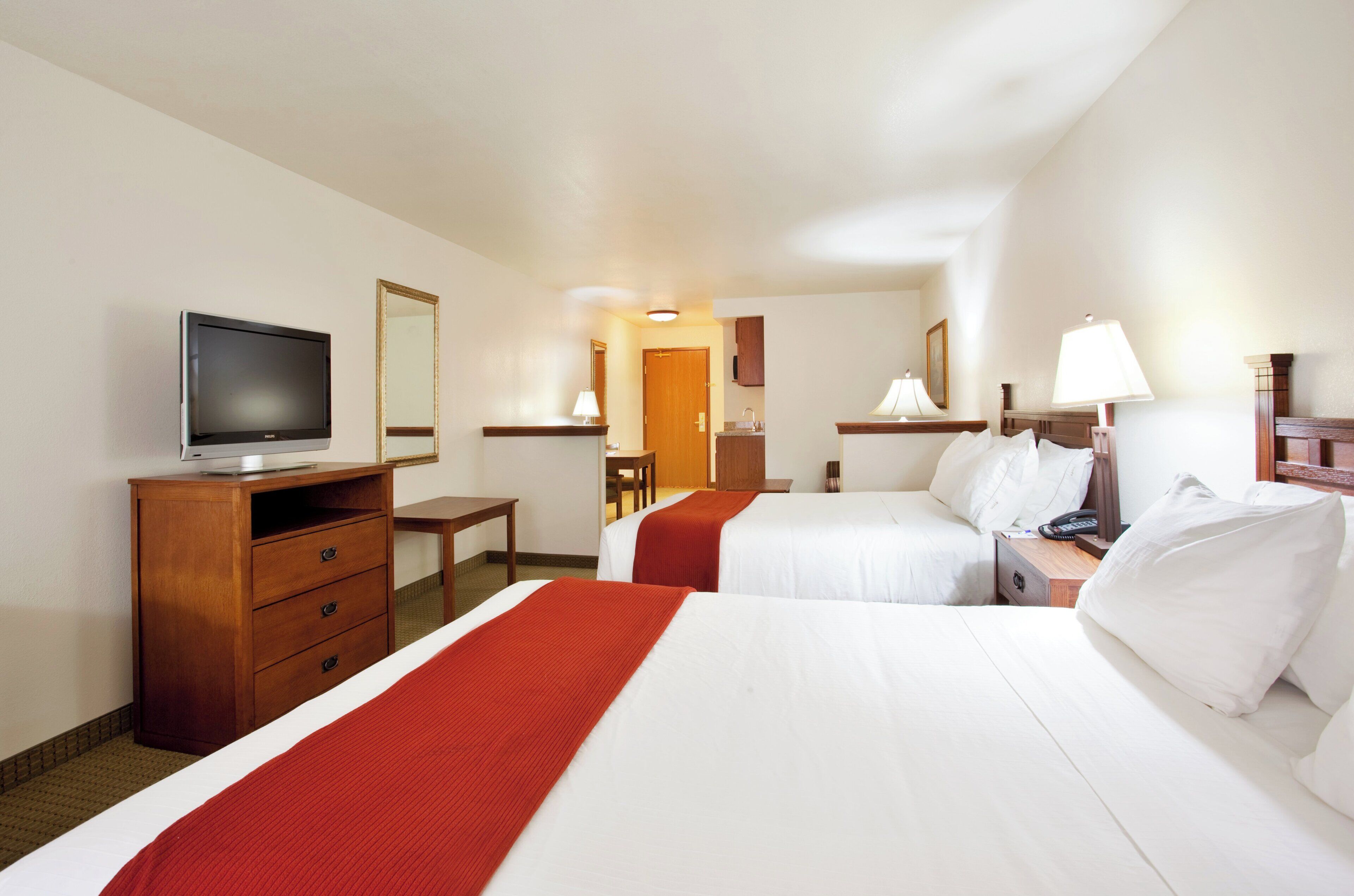 A hotel room with two beds, a TV, a desk, and a mirror.