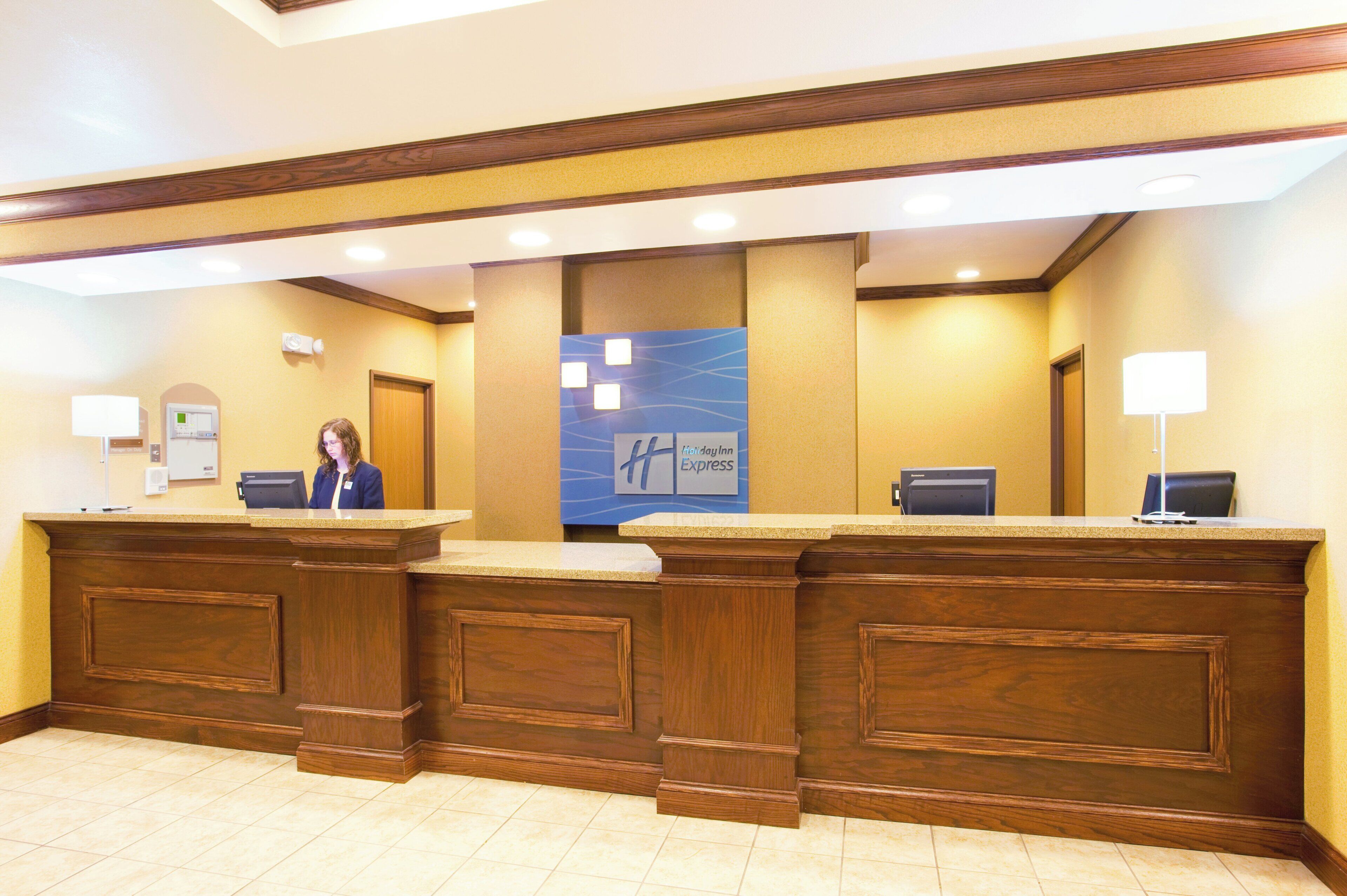 A hotel reception desk with a receptionist, a Holiday Inn Express sign, and a reception area with a tiled floor.