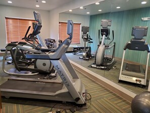 A gym with various exercise equipment including treadmills and stationary bikes, a mirrored wall, and a patterned carpet.