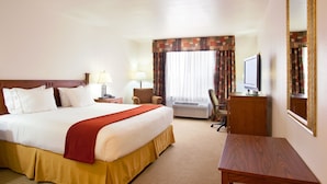 A hotel room with a large bed, a desk, a chair, a television, and a window with curtains.