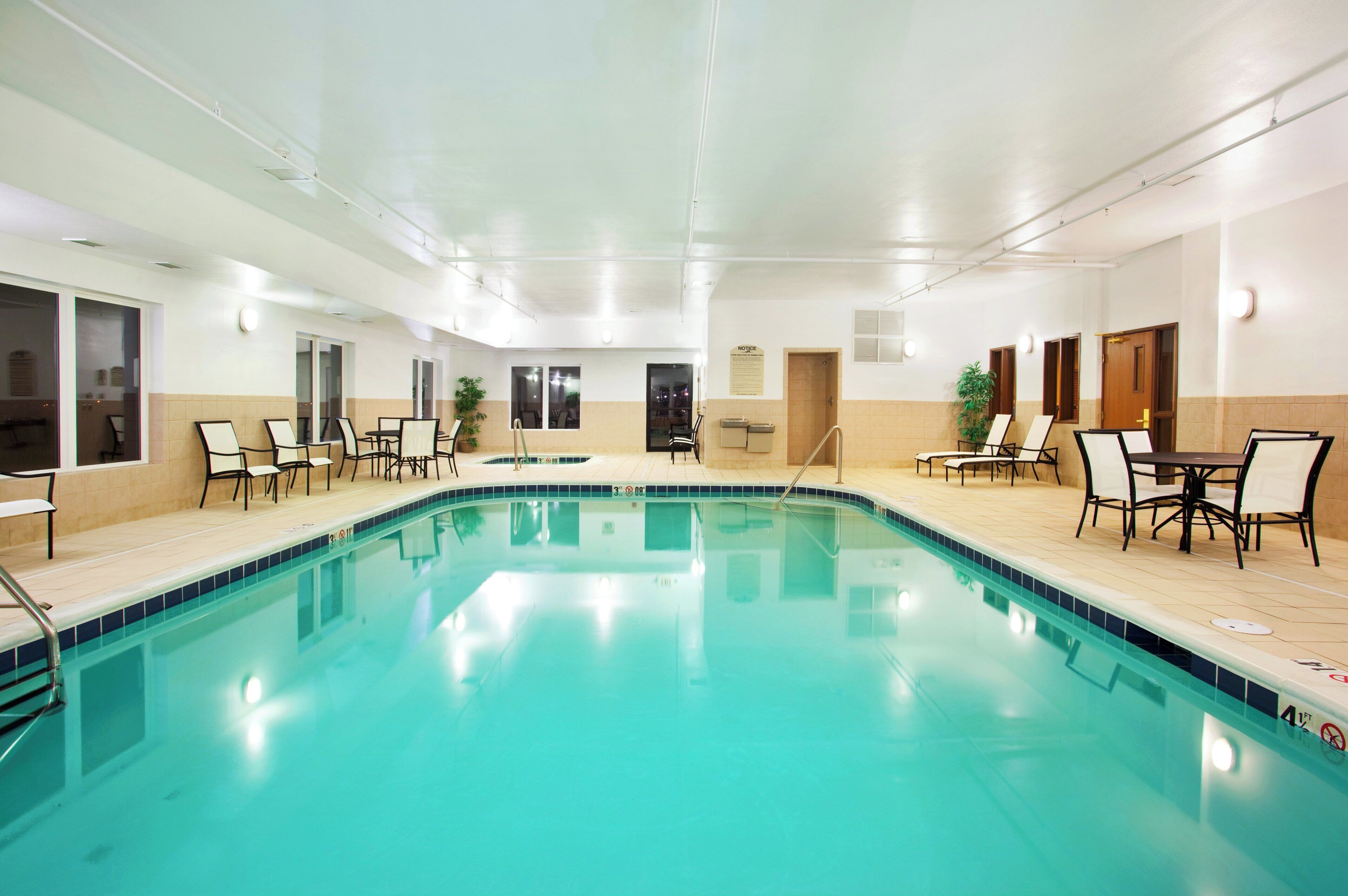 Piscina interna com água cristalina, rodeada por cadeiras de descanso e mesas.