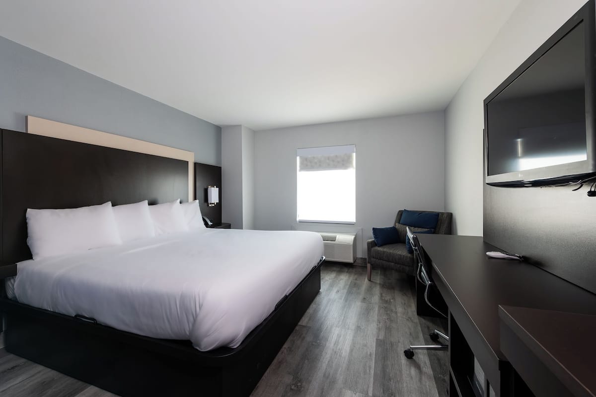 A modern hotel room with a large bed, a desk, a flat-screen TV, and a window providing natural light.