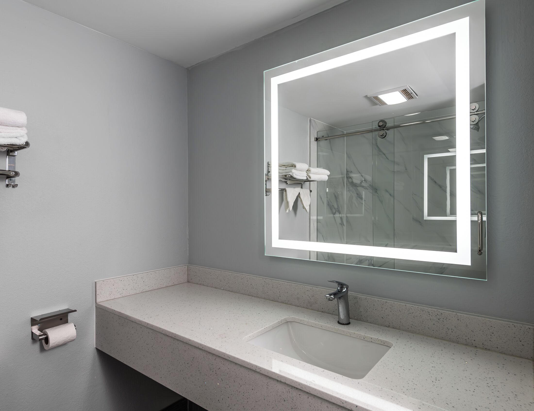 A modern bathroom with a large mirror, a sink, and a shower.