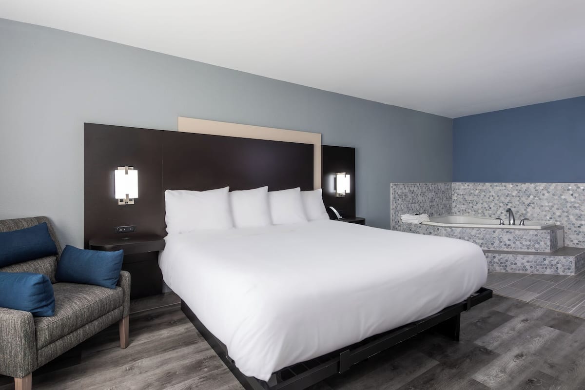 A modern hotel room with a large bed, a nightstand, a sofa, and a bathroom with a bathtub.