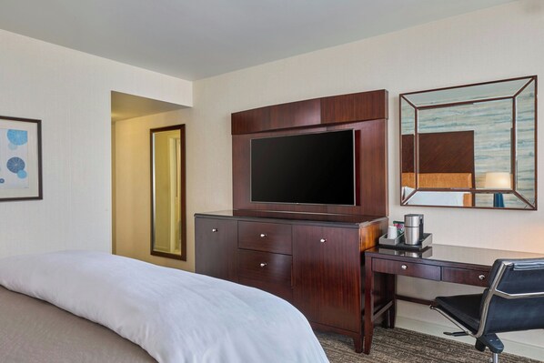 A hotel room with a bed, a desk, a television, a mirror, and a coffee maker.