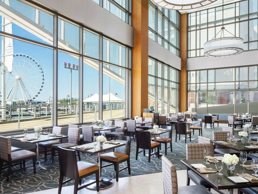 Un restaurante amplio con varias mesas y sillas, ventanas grandes que ofrecen vistas a una noria y al paseo marítimo.