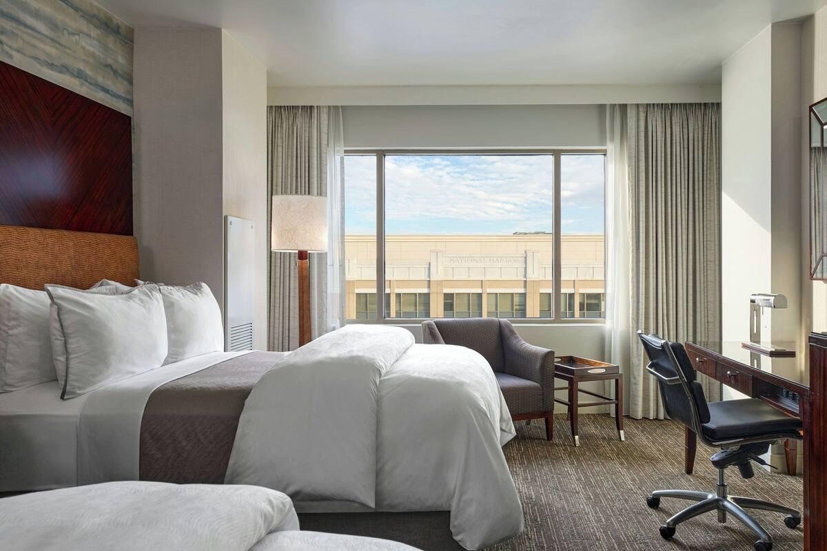 A hotel room with a large bed, a desk, a chair, and a view of a building.