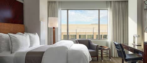 A hotel room with a large bed, a desk, a chair, and a view of a building.
