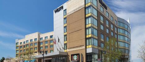 Um hotel moderno com uma cafeteria Starbucks no andar térreo, vários andares e céu claro.