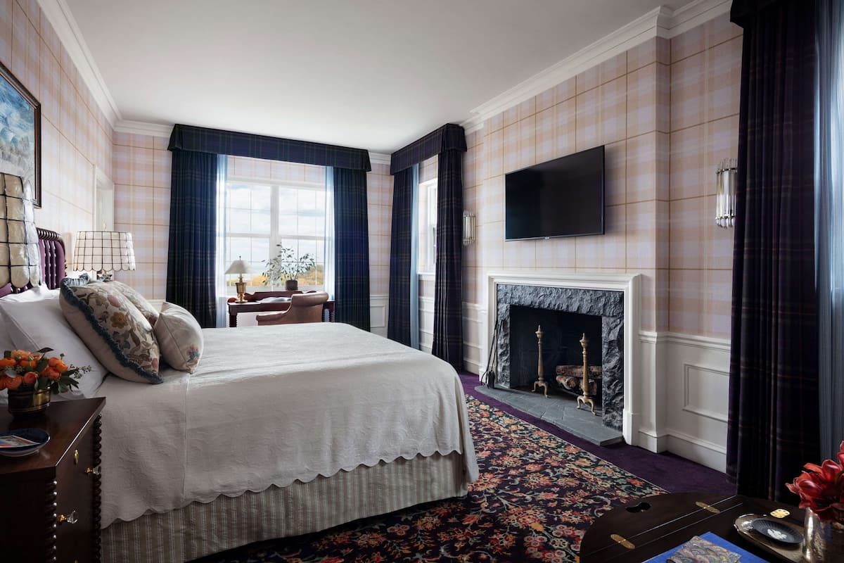 Un dormitorio con una cama grande, una chimenea, un televisor montado en la pared y vistas al exterior por la ventana.