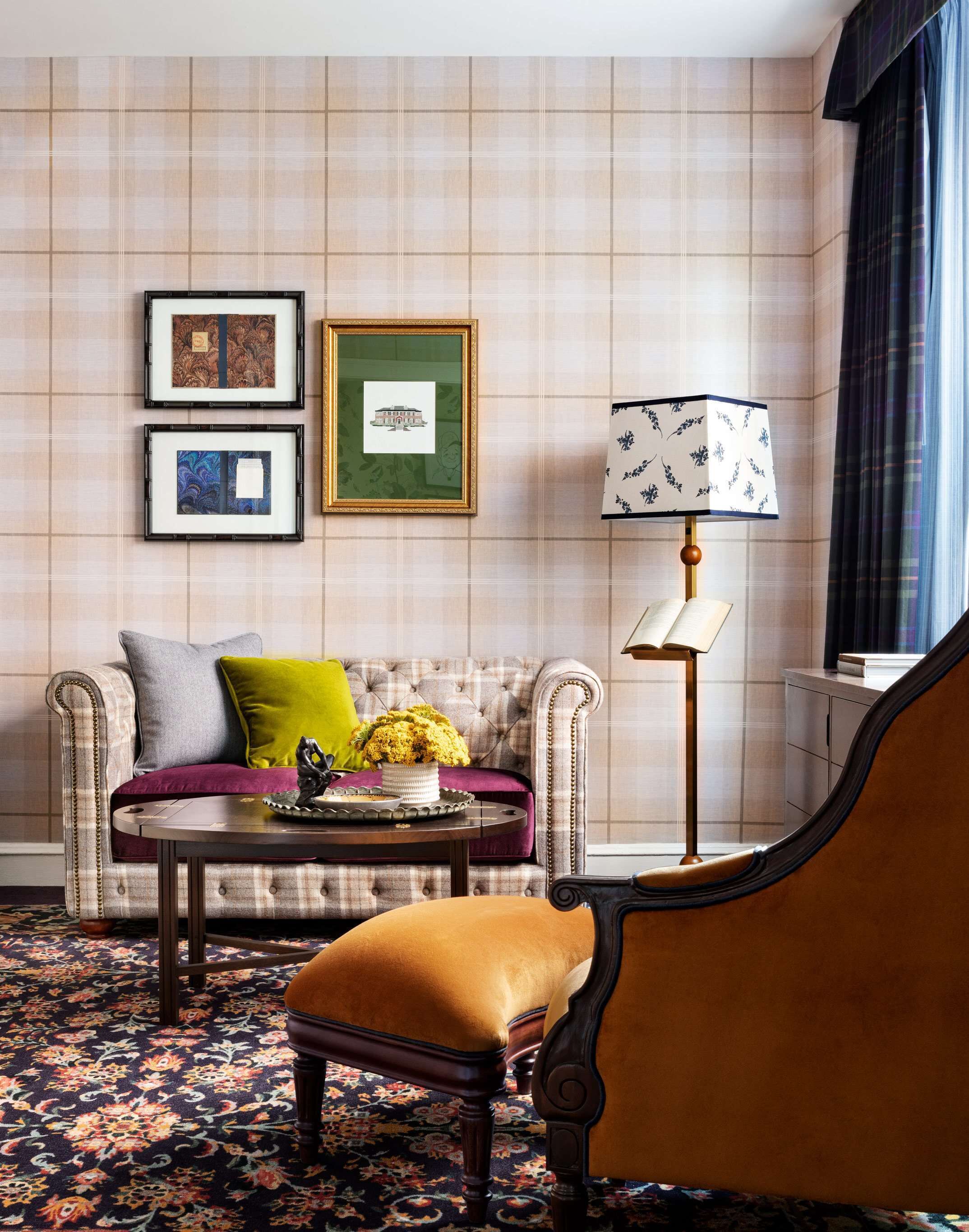A room with a tufted sofa, a round coffee table, a patterned rug, a lamp, and framed artwork on the wall.
