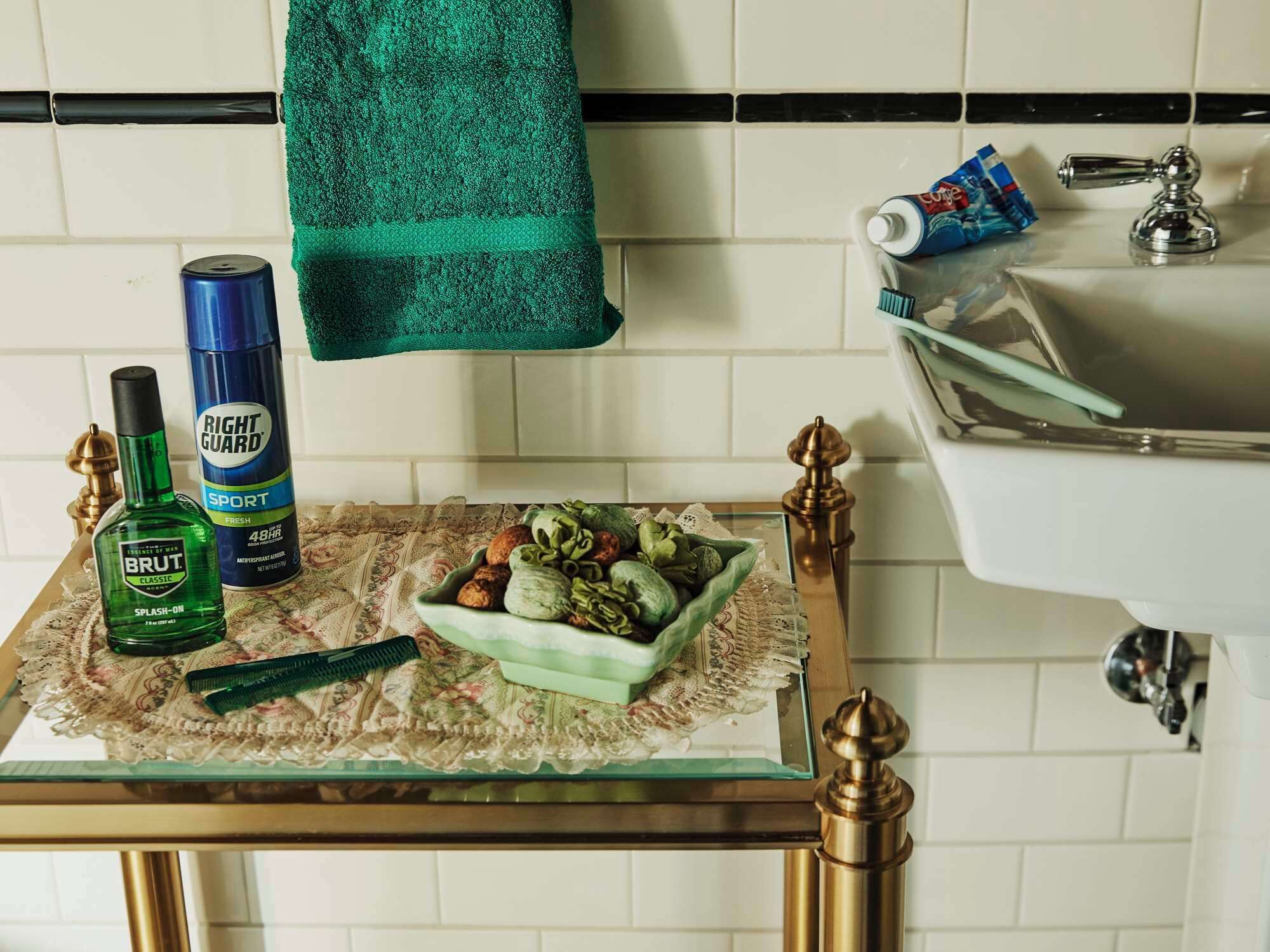 Un baño con lavamanos, una toalla verde y artículos de tocador sobre una mesita de cristal.