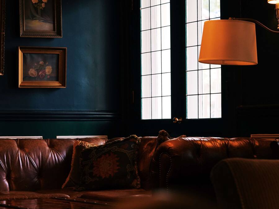 Una stanza blu scuro con un divano in pelle, opere d'arte incorniciate al muro e una lampada.
