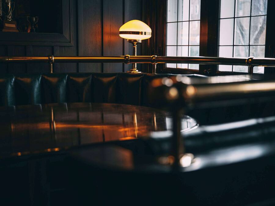 Un bar tenuemente iluminado con asientos de cuero y una lámpara de mesa.