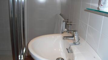 Un baño con un lavamanos blanco, grifo de cromo y un estante de vidrio sobre el lavamanos.