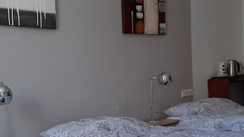 A bedroom with a large bed, a bedside table, a lamp, a wall art piece, and a small cabinet.