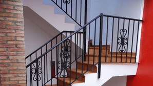 A multi-level staircase with black railings and terracotta steps, adjacent to a red wall and a brick column. - Hotel Ronda (Ronda)