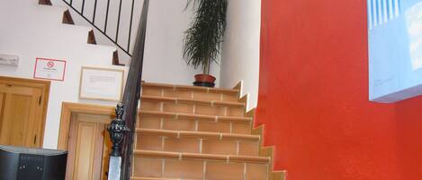 Una escalera con una pared roja, una planta en maceta y un certificado enmarcado en la pared.