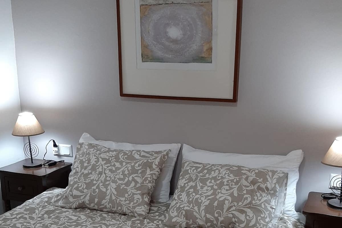 A neatly made bed with patterned bedding, two bedside tables with lamps, and a framed artwork above the bed.