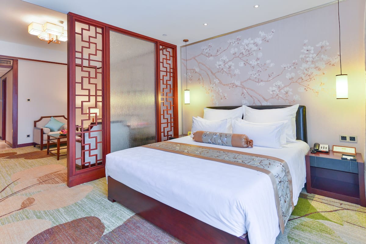 A hotel room with a bed, a nightstand, a chair, a decorative wall, and a traditional partition.