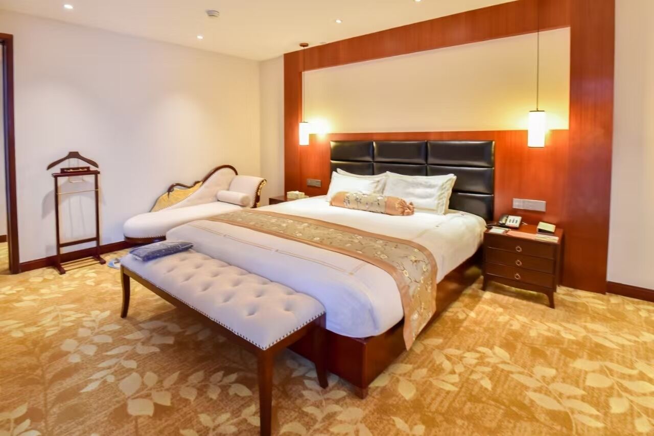 Une chambre d’hôtel avec un grand lit, une banquette, une table de chevet et une lampe fixée au mur.