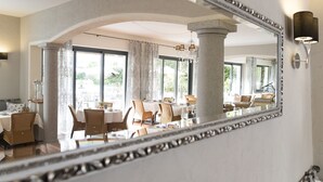 A dining area with a large mirror reflecting the room, featuring a chandelier, dining tables, and chairs. - Boutique-Hotel REMORINO (Minusio)