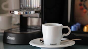 A white Nespresso cup on a saucer next to a black coffee machine.
