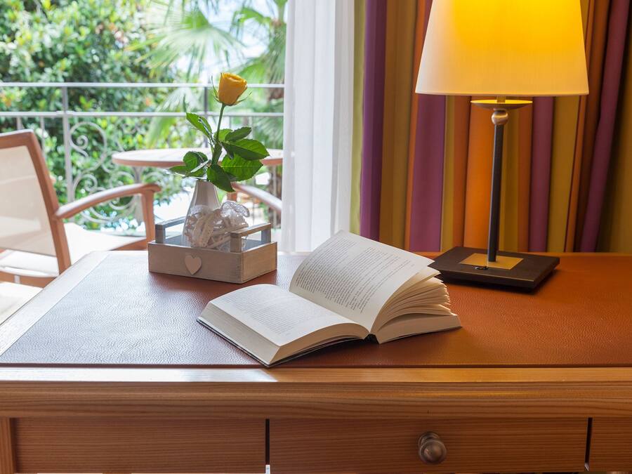 Een houten bureau met een open boek, een vaas met een enkele gele roos, en een lamp.