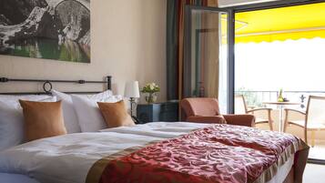 A hotel room with a large bed, a desk with a lamp, a chair, and a balcony with a yellow umbrella.