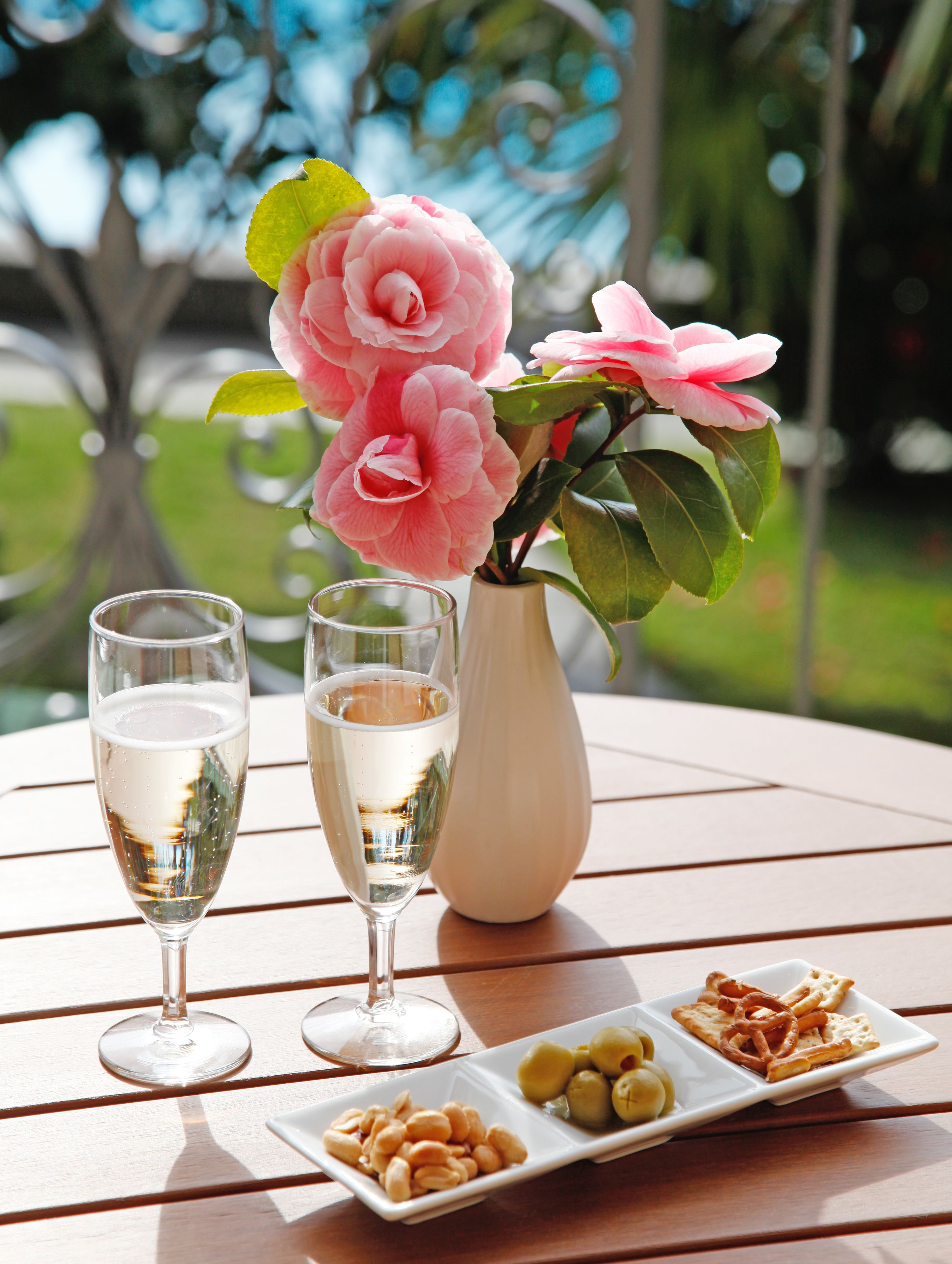 A table with two champagne glasses, a vase with pink flowers, and a plate with olives and crackers.