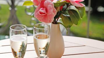 A table with two champagne glasses, a vase with pink flowers, and a plate with olives and crackers.