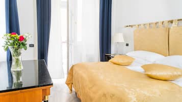 Una camera d'albergo con un letto, un comodino, una lampada, un vaso con fiori e tende.