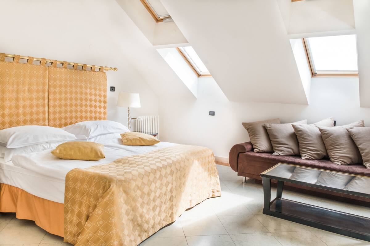A bedroom with a large bed, a sofa, and skylights.